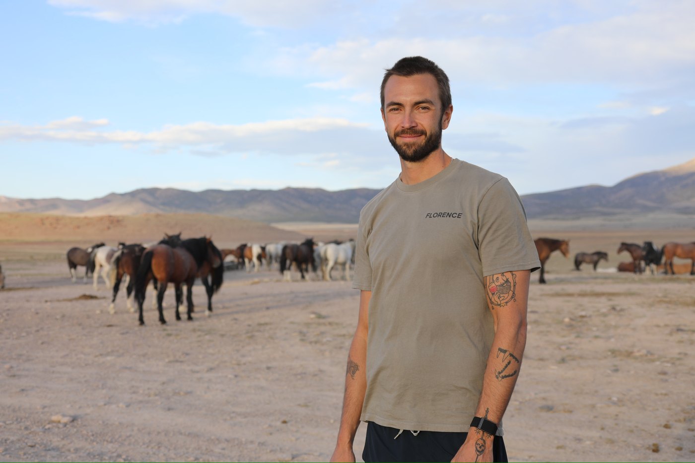 Josh standing in the Utah west desert with a band of wild horses behind him